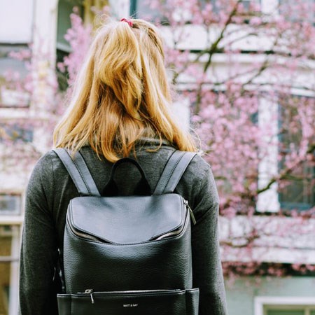 Dziewczyna o blond włosach z czarnym plecakiem patrząca na kwitnącą wiśnię