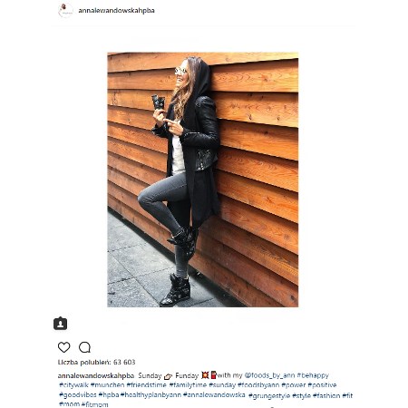 Anna Lewandowska w czarnej ramonesce oparta o drewnianą ścianę
