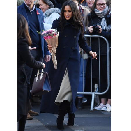 Meghan Markle w granatowym płaszczu i czarnych kozakach z bukietem kwiatów w ręce