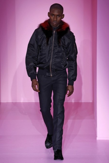 Model z pokazu Givenchy ubrany w grafitowe spodnie w kant i czarną kurtkę typu bomber z czerwonym futrem.