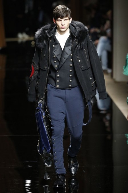 Model z pokazu Balmain w militarnej kurtce z futrem i granatowych spodniach na zatrzaski.