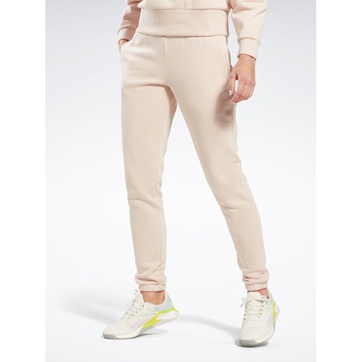 Reebok Spodnie dresowe Fleece IC3502 Beżowy Slim Fit ze sklepu MODIVO w kategorii Spodnie damskie - zdjęcie 182701658