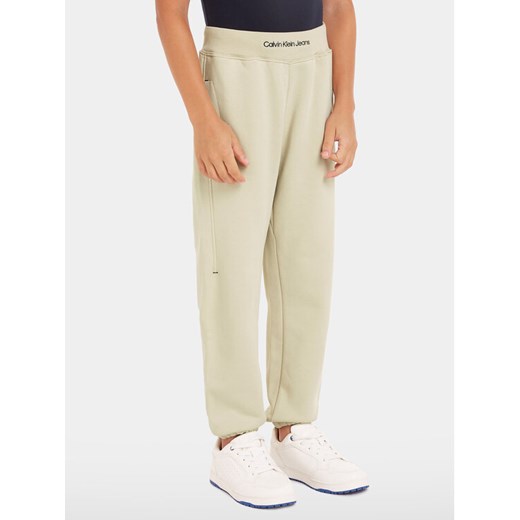Calvin Klein Jeans Spodnie dresowe Intrasia Logo IB0IB02081 Beżowy Regular Fit ze sklepu MODIVO w kategorii Spodnie chłopięce - zdjęcie 182714766