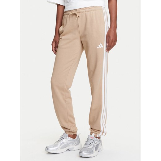 adidas Spodnie dresowe Essentials 3-Stripes JX7661 Beżowy Regular Fit ze sklepu MODIVO w kategorii Spodnie damskie - zdjęcie 184231806