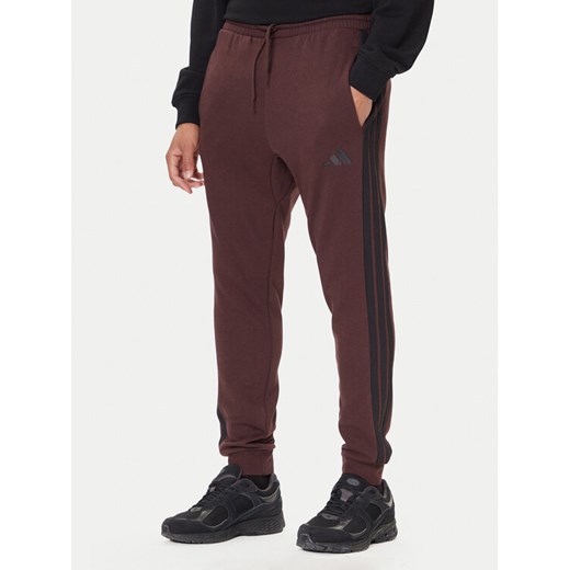 adidas Spodnie dresowe Essentials 3-Stripes JX0749 Brązowy Regular Fit ze sklepu MODIVO w kategorii Spodnie męskie - zdjęcie 186086868