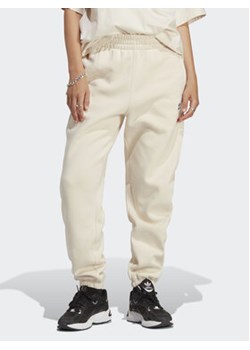 adidas Spodnie dresowe Essentials Fleece IA6436 Écru Regular Fit ze sklepu MODIVO w kategorii Spodnie damskie - zdjęcie 168524129