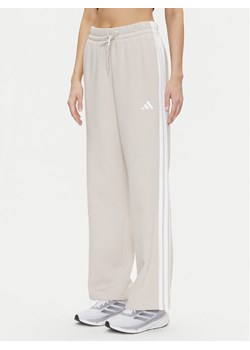 adidas Spodnie dresowe Essentials 3-Stripes JW9215 Beżowy Regular Fit ze sklepu MODIVO w kategorii Spodnie damskie - zdjęcie 181140835