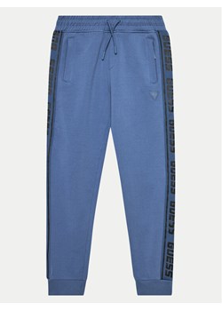 Guess Spodnie dresowe L2YQ48 K6ZS1 Niebieski Relaxed Fit ze sklepu MODIVO w kategorii Spodnie chłopięce - zdjęcie 181189199
