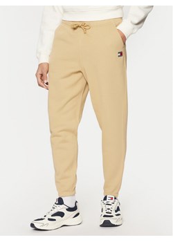 Tommy Jeans Spodnie dresowe Badge DM0DM20276 Beżowy Regular Fit ze sklepu MODIVO w kategorii Spodnie męskie - zdjęcie 182690158