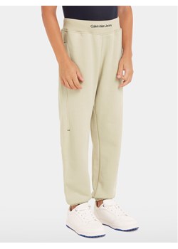Calvin Klein Jeans Spodnie dresowe Intrasia Logo IB0IB02081 Beżowy Regular Fit ze sklepu MODIVO w kategorii Spodnie chłopięce - zdjęcie 182714766