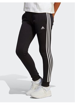 adidas Spodnie dresowe Essentials 3-Stripes French Terry Cuffed Joggers IC8770 Czarny Slim Fit ze sklepu MODIVO w kategorii Spodnie damskie - zdjęcie 183757316