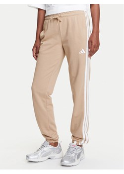 adidas Spodnie dresowe Essentials 3-Stripes JX7661 Beżowy Regular Fit ze sklepu MODIVO w kategorii Spodnie damskie - zdjęcie 184231806