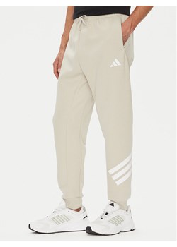 adidas Spodnie dresowe Future Icons 3-Stripes JW7092 Beżowy Regular Fit ze sklepu MODIVO w kategorii Spodnie męskie - zdjęcie 184632578