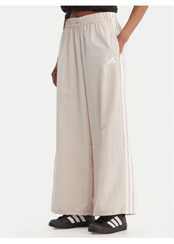 adidas Spodnie dresowe Essentials 3-Stripes JC8168 Beżowy Loose Fit ze sklepu MODIVO w kategorii Spodnie damskie - zdjęcie 188515125